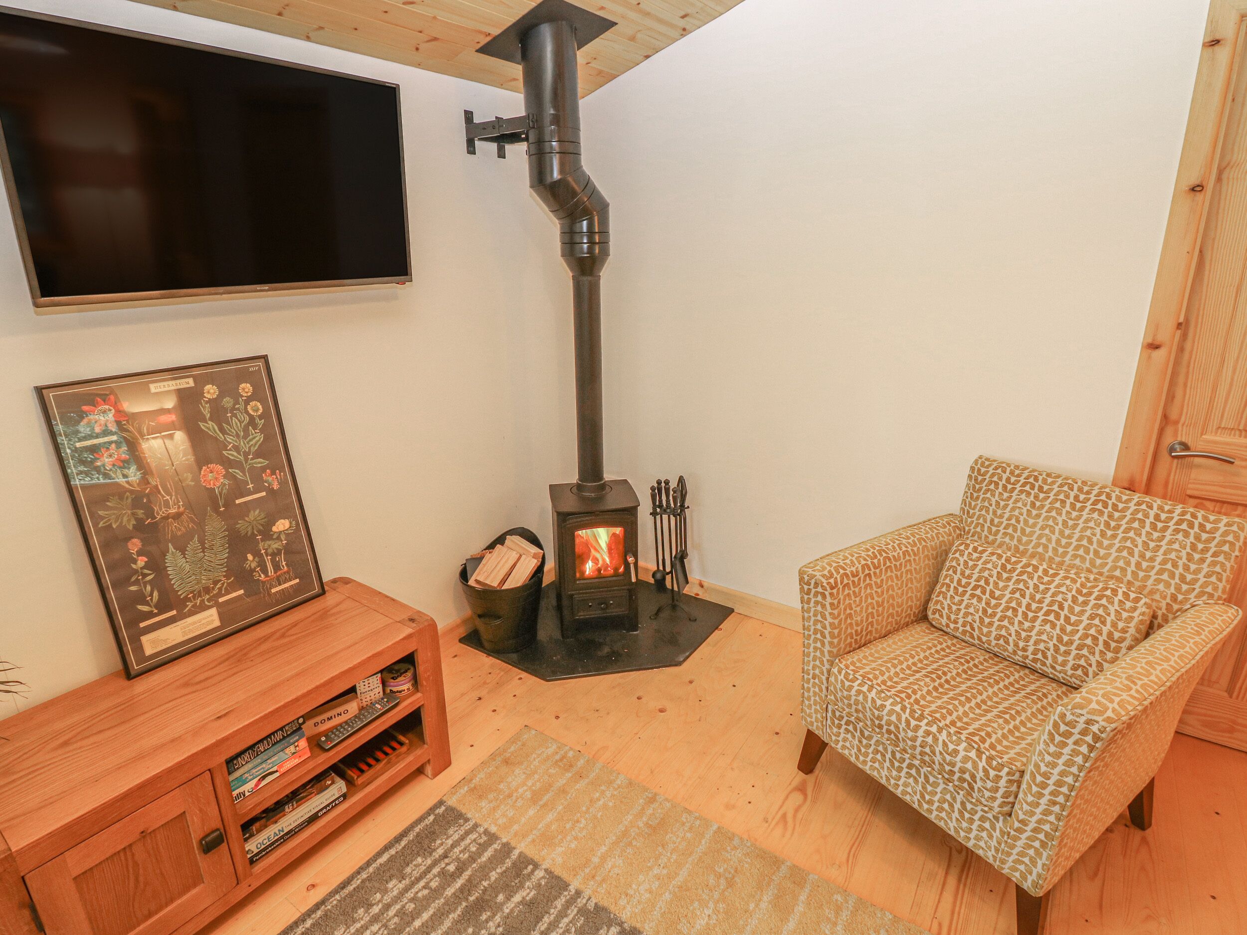 A cozy living room with a fireplace, a sofa, a TV mounted on the wall, and a wooden cabinet with books.