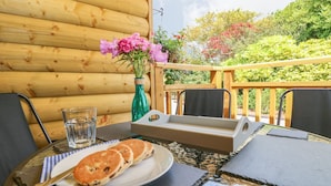 Une terrasse en bois avec une table mise pour le petit-déjeuner, comprenant des crêpes et un verre d’eau.