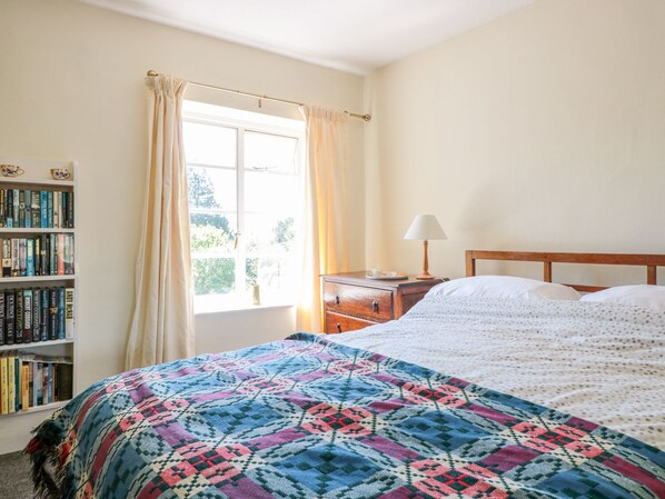 A bedroom with a bed, a bedside table with a lamp, a window with curtains, and a bookshelf filled with books. - 7 Glendower Street (Monmouth)