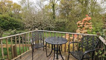 A wooden deck with a table and chairs, surrounded by a wooden fence and various trees and shrubs.