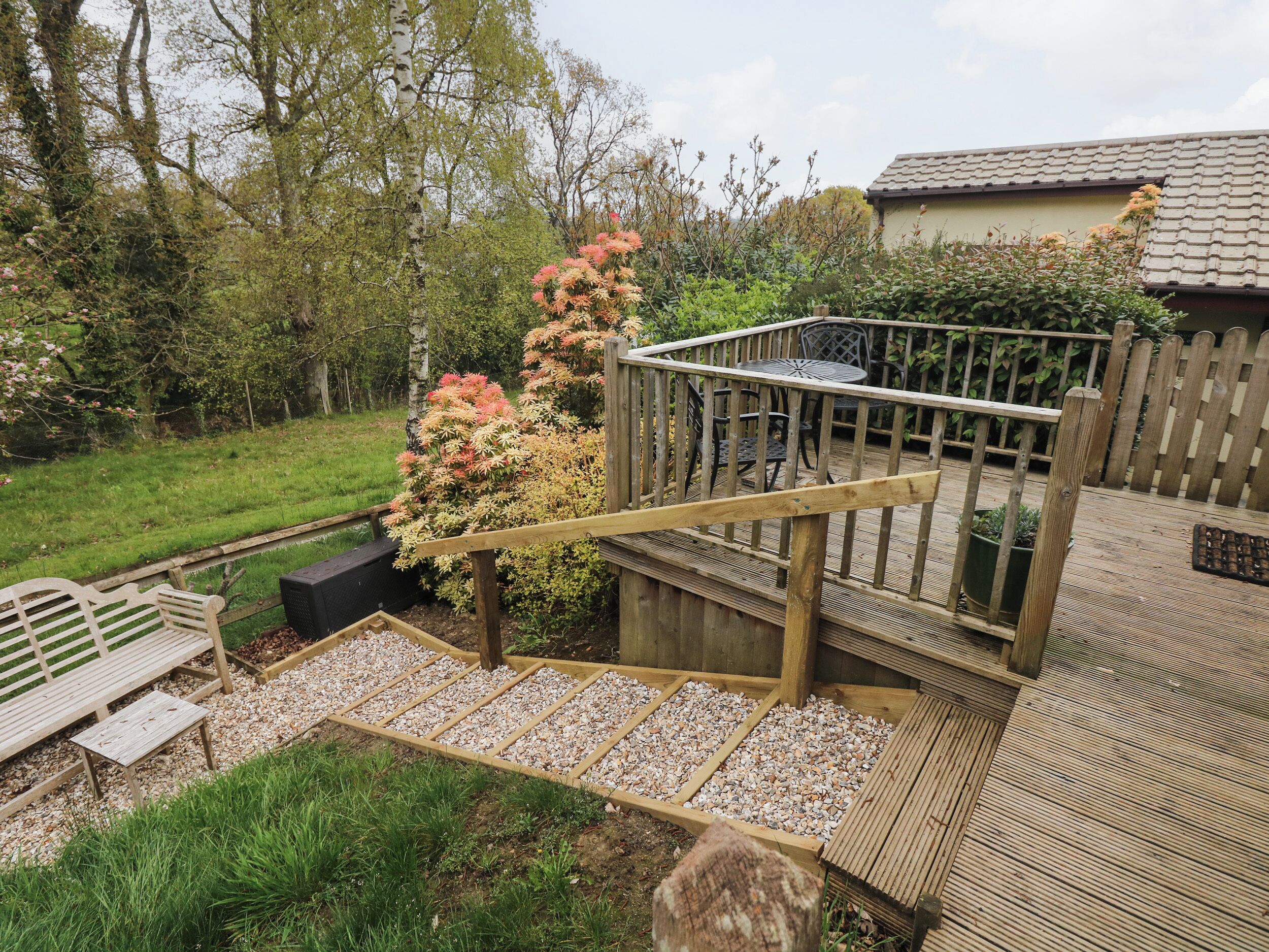 Een houten terras met een metalen reling, omringd door groen en een kleine tuin.