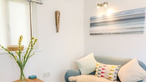 A cozy living room with a blue sofa, a wooden side table with a vase of flowers, and a painting on the wall.