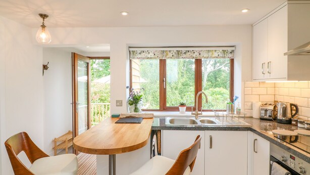 A modern kitchen with a wooden table, two chairs, a sink, and a window with a view of greenery.