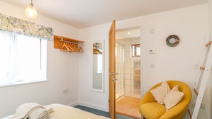 A bedroom with a bed, a chair, a wardrobe, and a bathroom visible through an open door.
