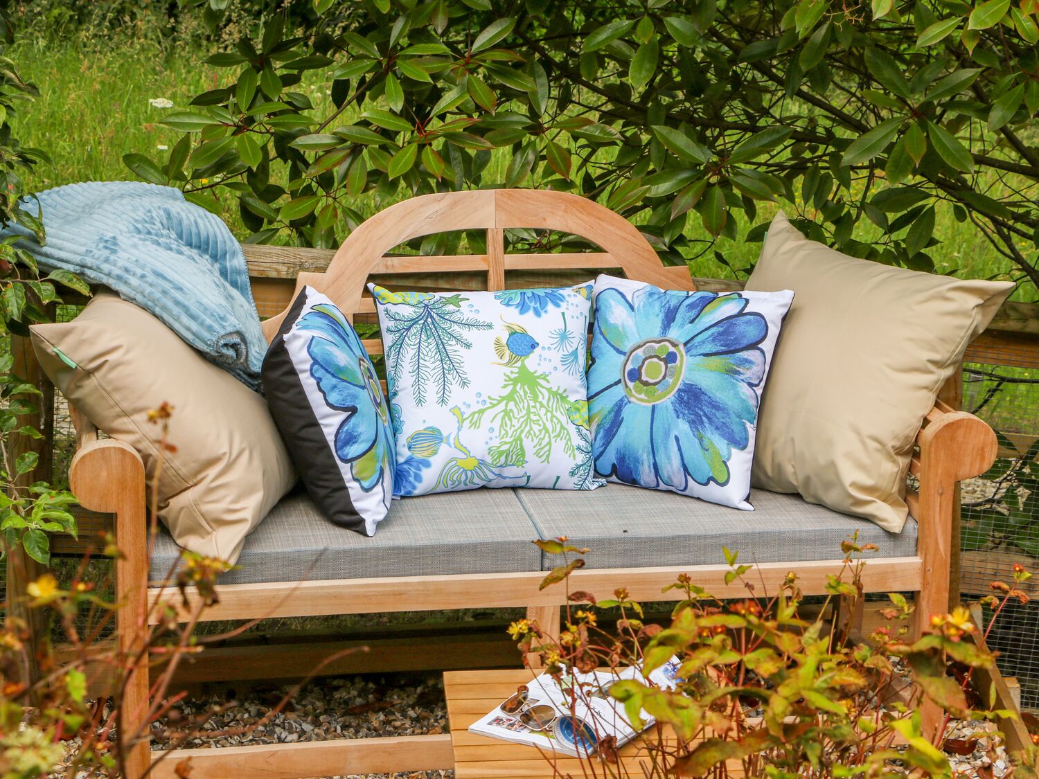 A wooden bench with cushions, surrounded by greenery.