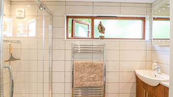 Un baño moderno con cabina de ducha de vidrio, un perchero con una toalla color beige, una ventana con vistas a la vegetación y un tocador de madera con un lavabo.