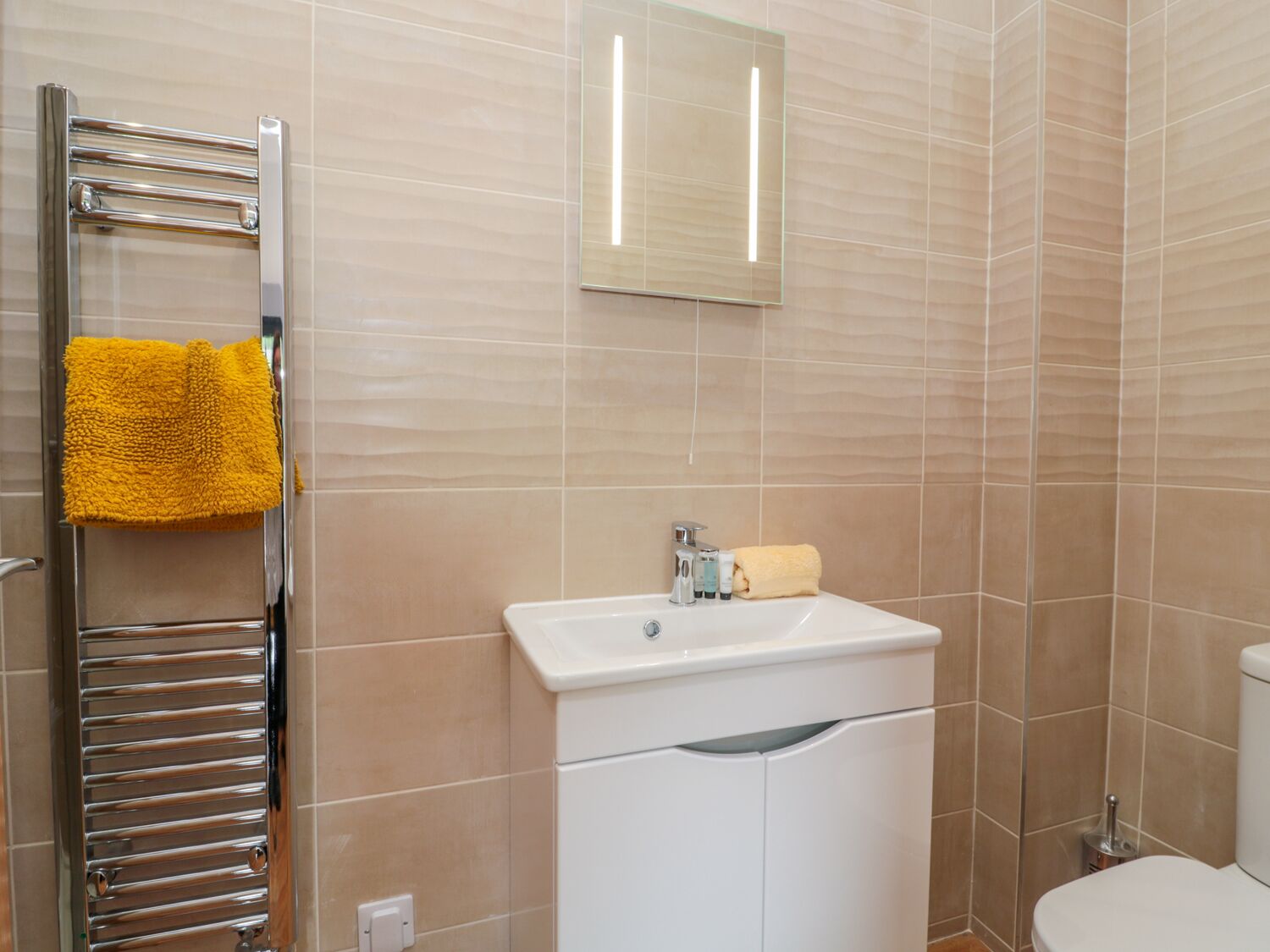 Un baño con toallero de cromo, un lavabo blanco, un espejo y un inodoro.