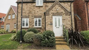 A two-story house with a brick facade, a white door, and a small front garden with various shrubs. - Causeway Cottage (Filey)