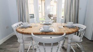 A dining area with a round wooden table set for four, surrounded by white chairs. - Causeway Cottage (Filey)
