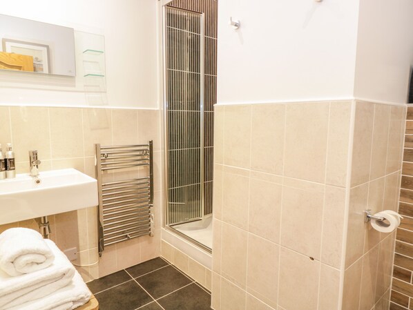 A bathroom with a sink, mirror, towel rack, shower, and toilet paper holder. - Penthouse St. Mary's Church (Moffat)