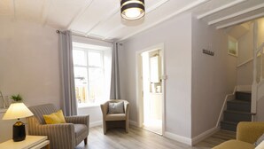 Una sala de estar con sofá, sillón, reposapiés, una lámpara y una ventana con cortinas.