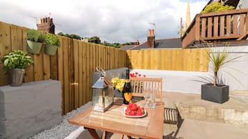 Enjoy a romantic meal on the patio surrounded by lush greenery and a charming wooden fence.