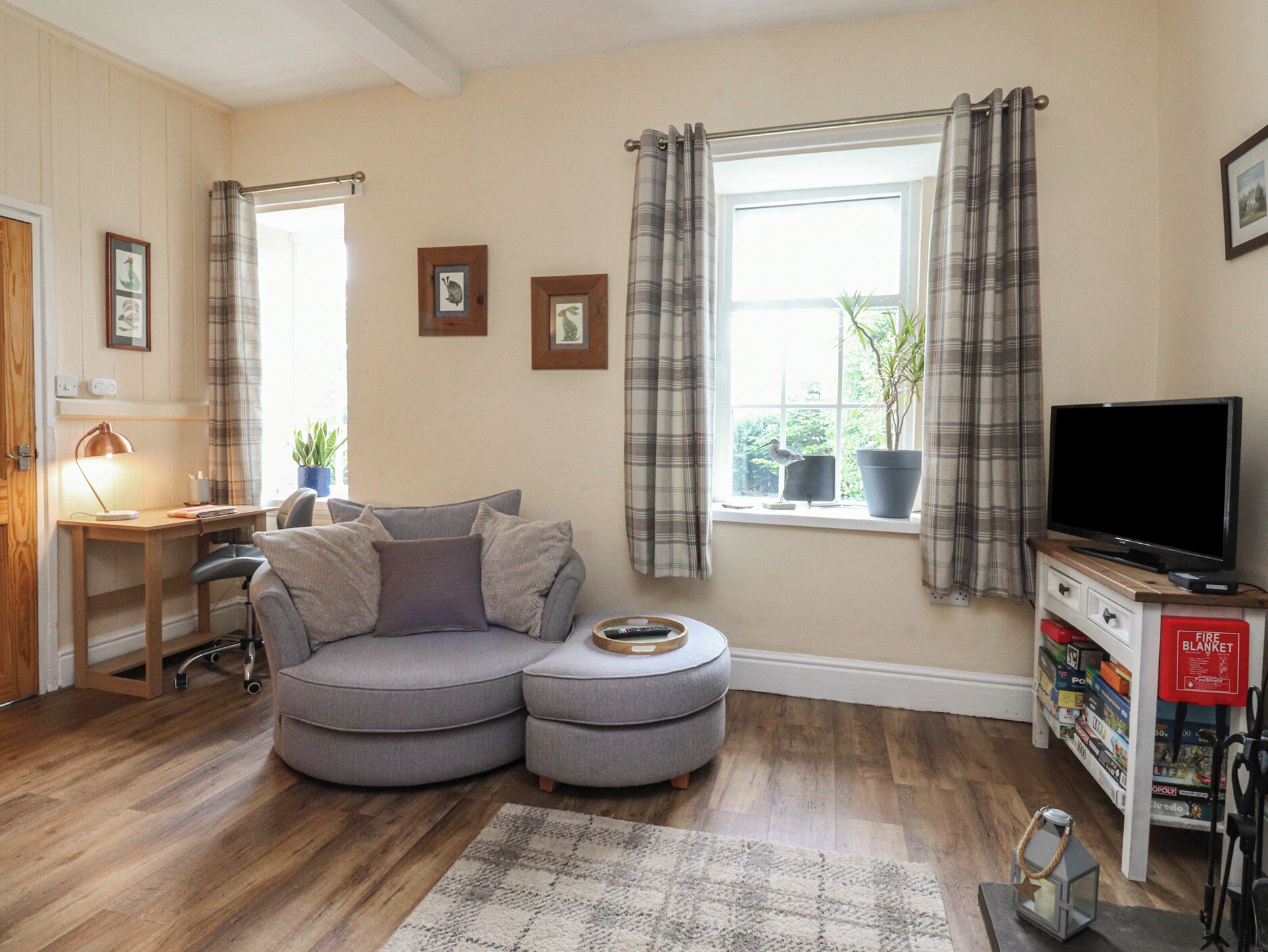 A cozy living room with a grey sectional sofa, a wooden desk, a television, and a bookshelf.