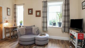 A cozy living room with a grey sectional sofa, a wooden desk, a television, and a bookshelf.