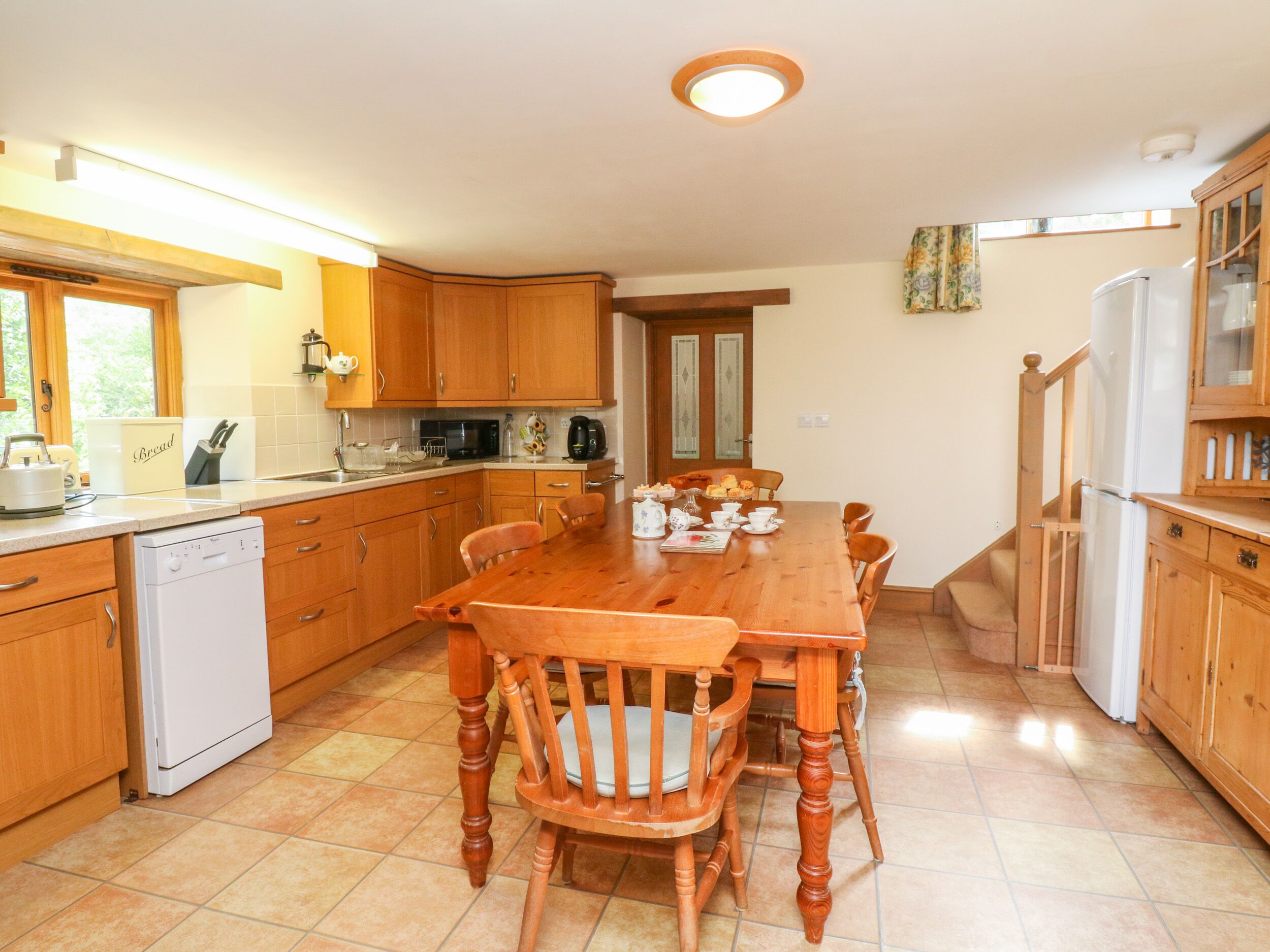 Une cuisine avec des meubles de rangement en bois, une table à manger, des chaises, un lave-vaisselle et un réfrigérateur.