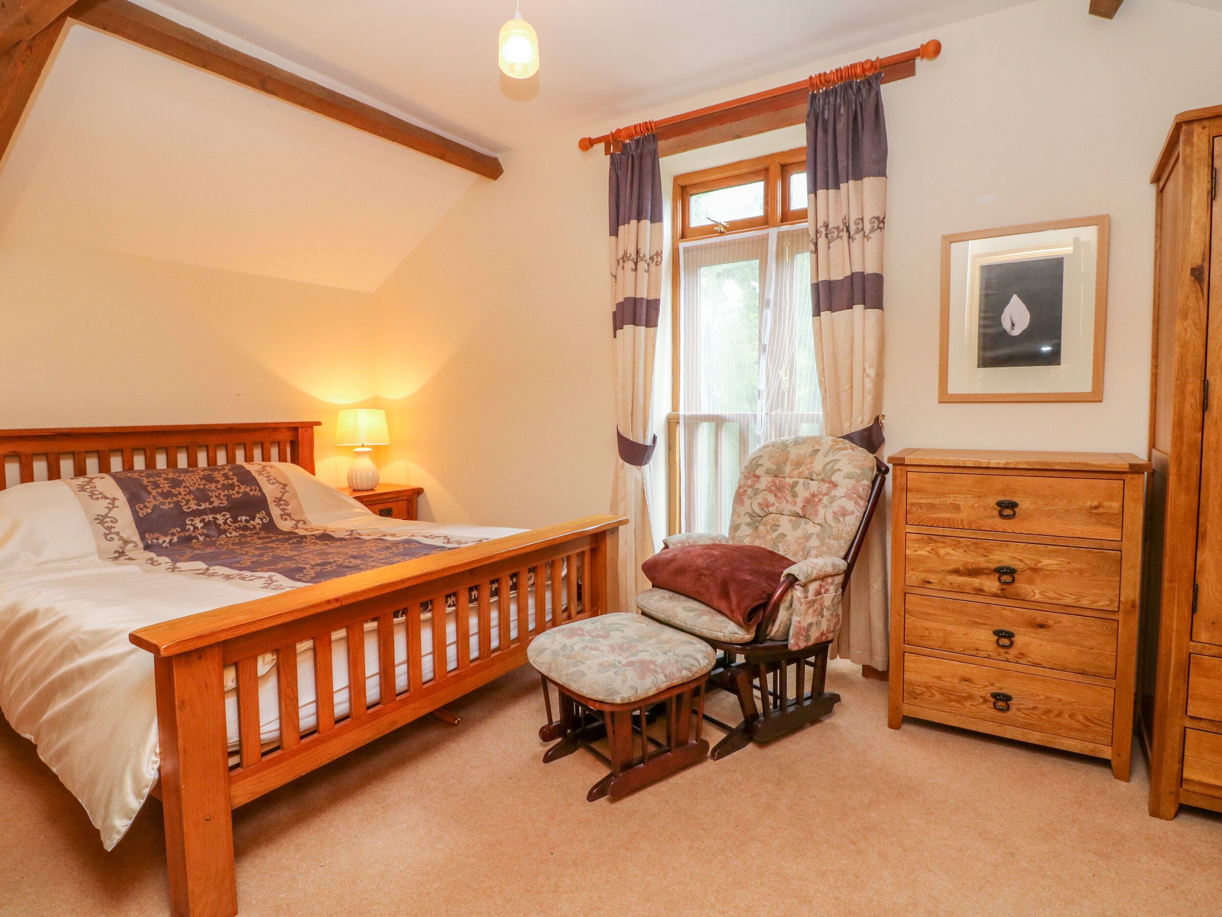Une chambre à coucher avec un lit en bois, une chaise, une commode et une fenêtre avec des rideaux.