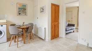 Un espace de vie compact comprenant un coin repas, un lave-linge et un canapé gris dans la pièce adjacente.