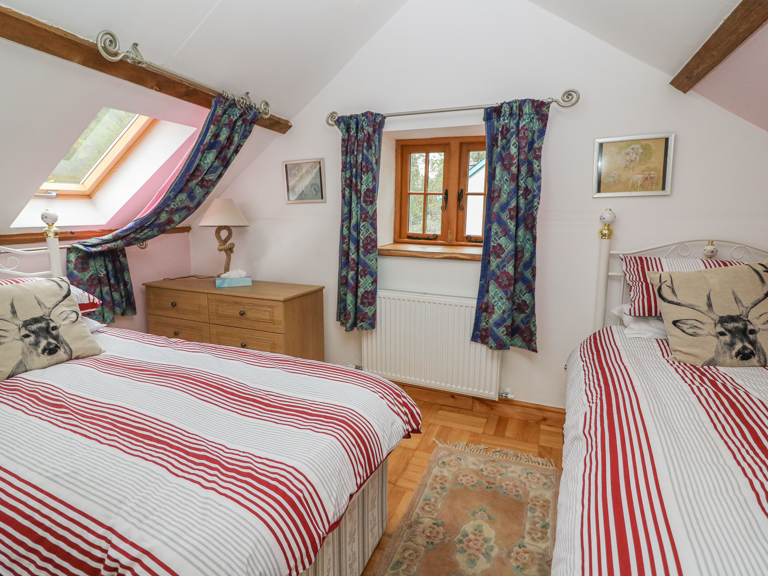 Une chambre avec deux lits, une commode, une fenêtre avec des rideaux, un radiateur et une lucarne.