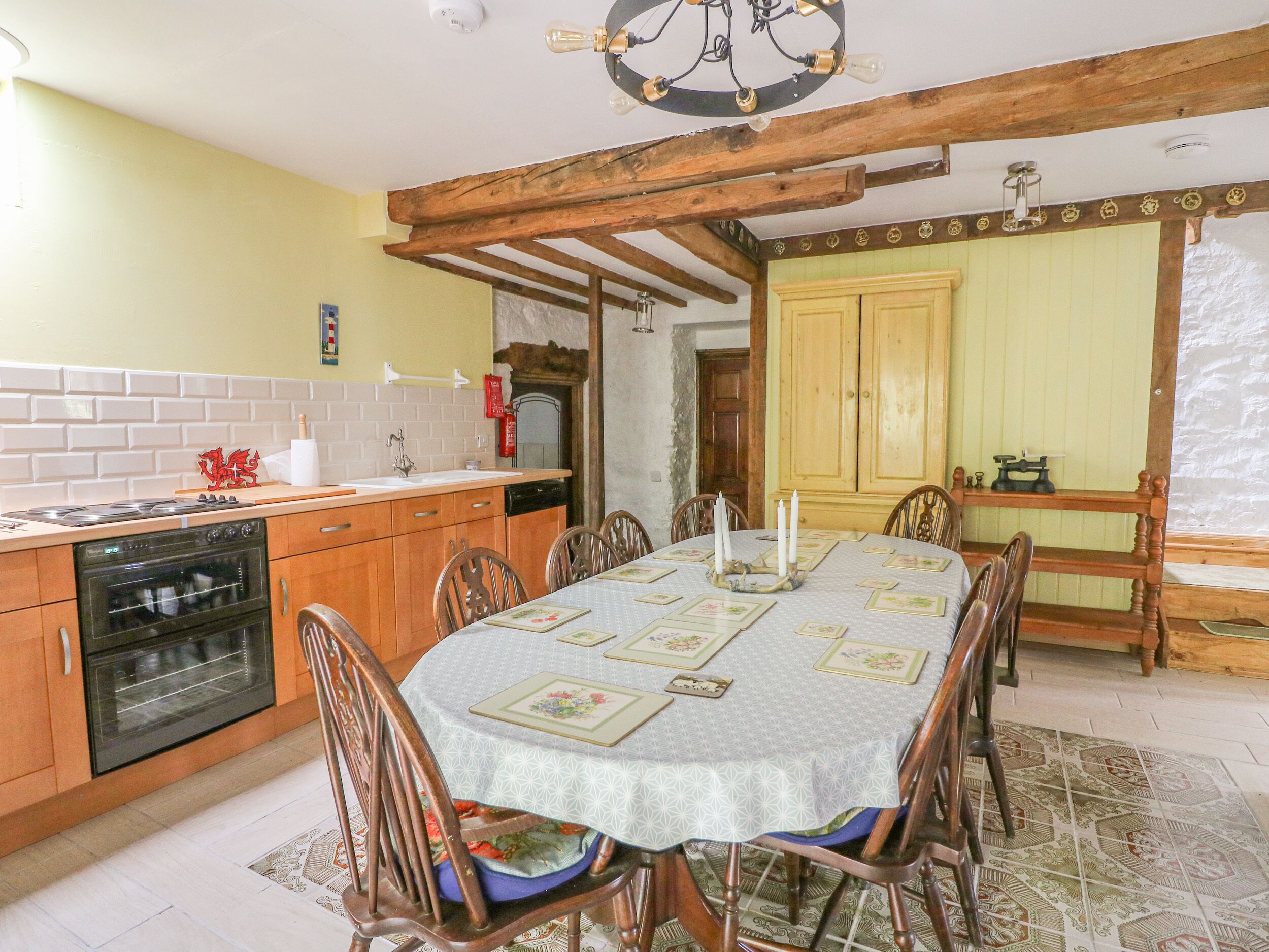 A dining area with a table set for six, surrounded by wooden chairs. There is a kitchen with a stove, oven, and sink in the background.