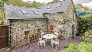 A stone building with a sloped roof, a wooden fence, and a patio area with a table and chairs. - Felin Iago (Aberystwyth)