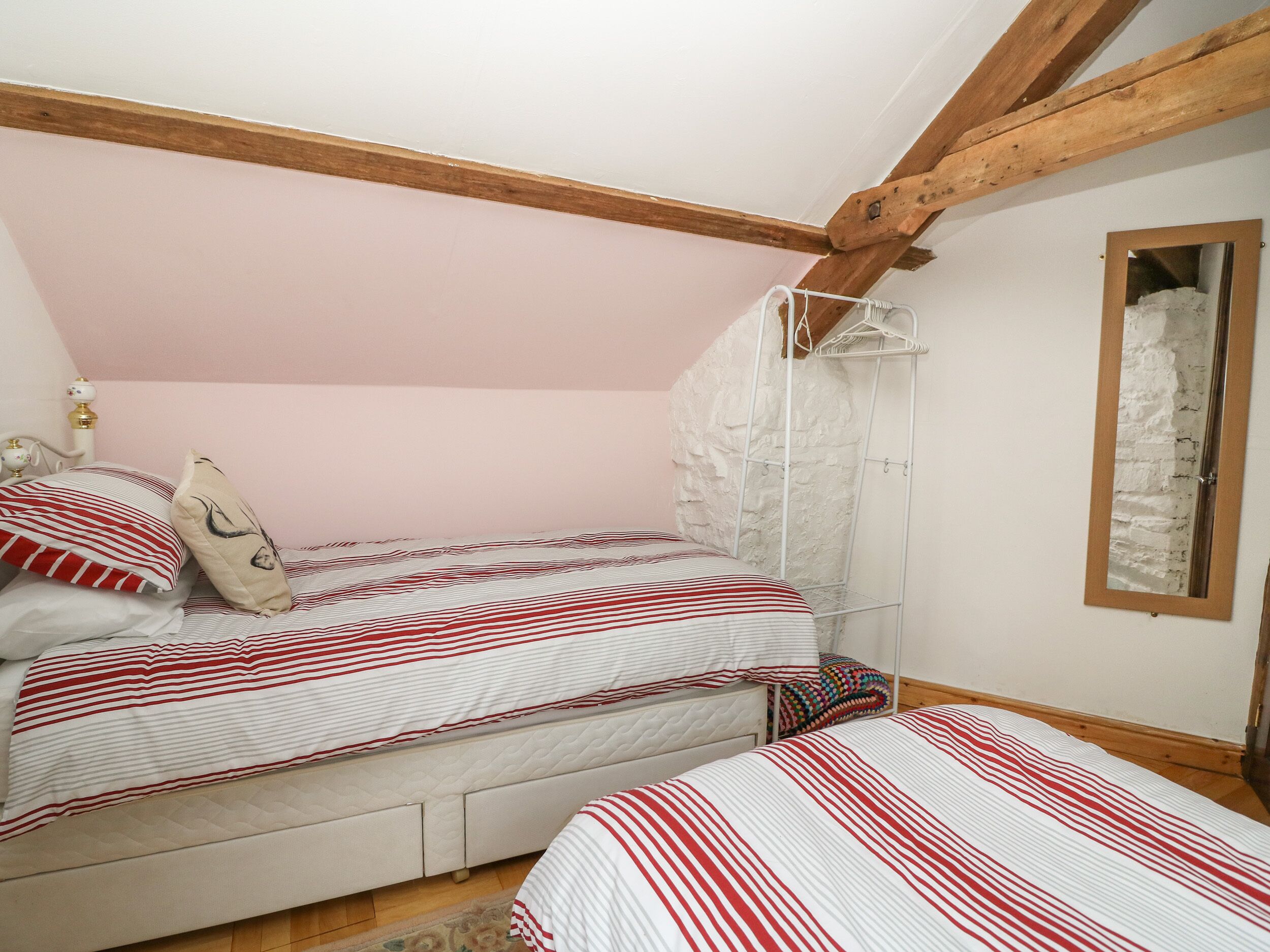 A bedroom with two beds, a wooden ceiling, a white brick wall, and a mirror.