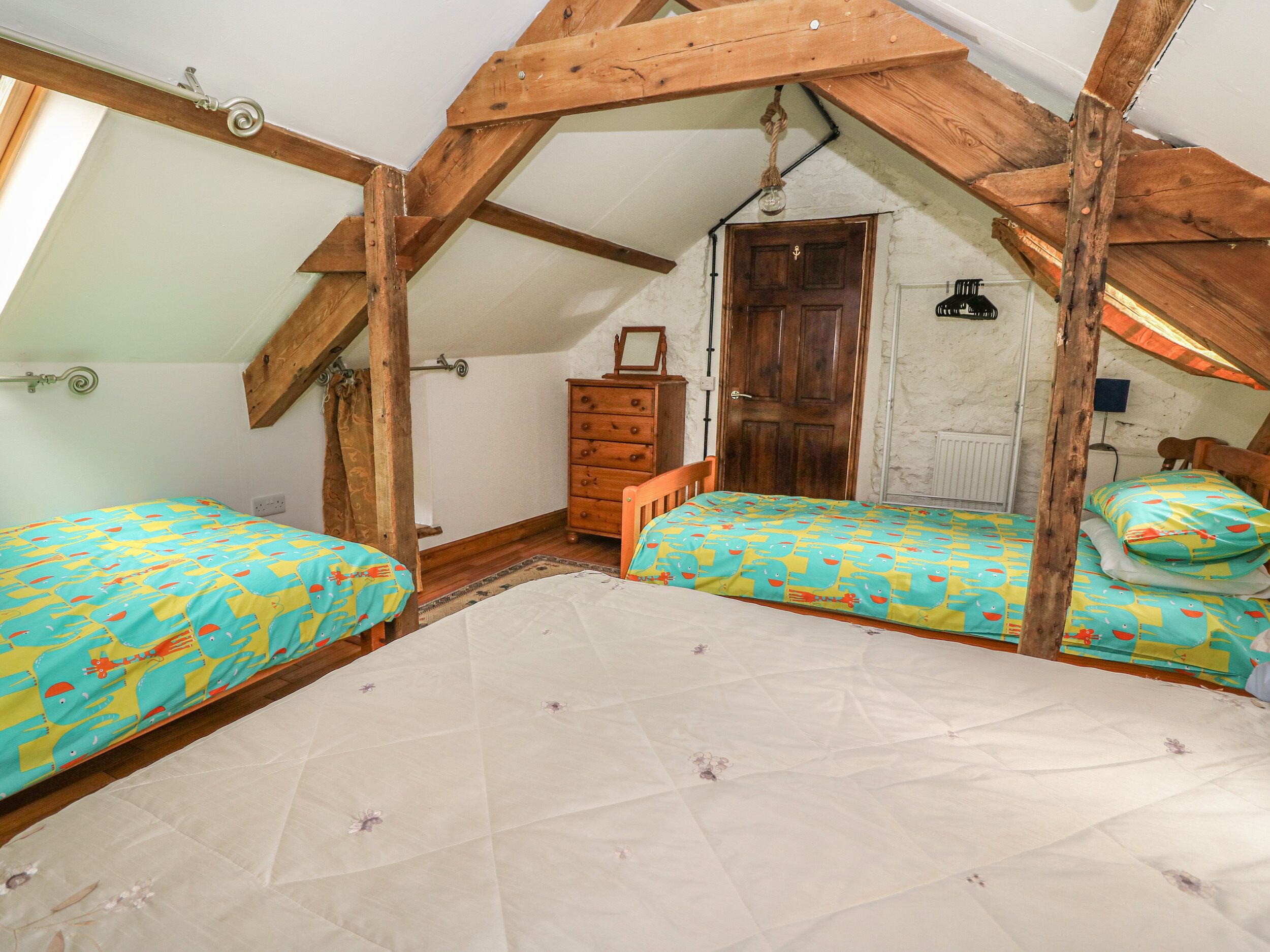 Un dormitorio pequeño en el ático con dos camas, vigas de madera, un aparador y una puerta.