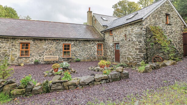 A stone building with a sloped roof, wooden windows, and a stone pathway leading to the entrance. - Felin Iago (Aberystwyth)