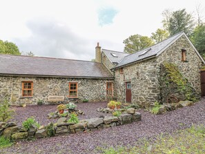 A stone building with a sloped roof, wooden windows, and a stone pathway leading to the entrance. - Felin Iago (Aberystwyth)
