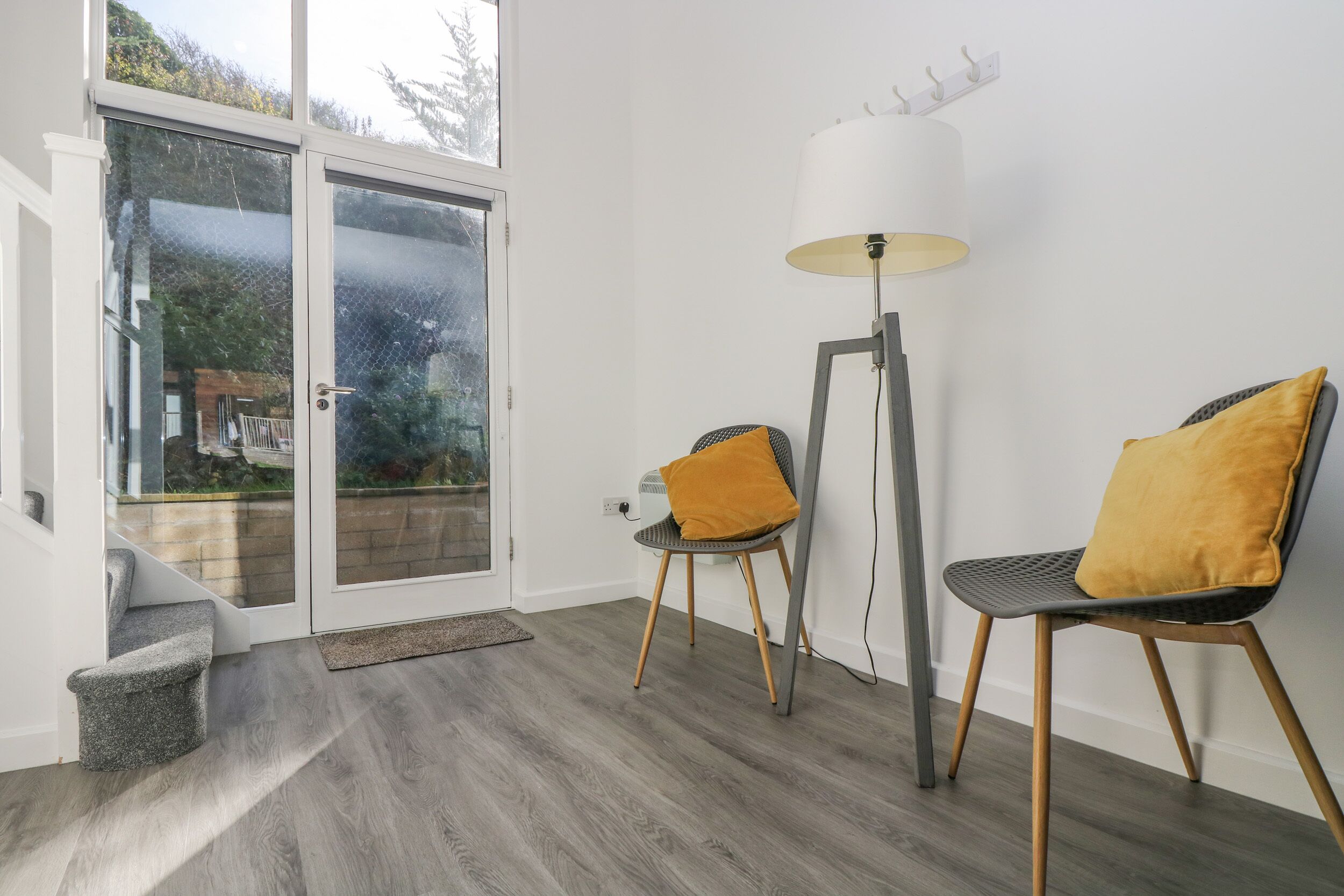 Un interior moderno con un ventanal de vidrio que da a un balcón, dos sillones con cojines y una lámpara de pie.