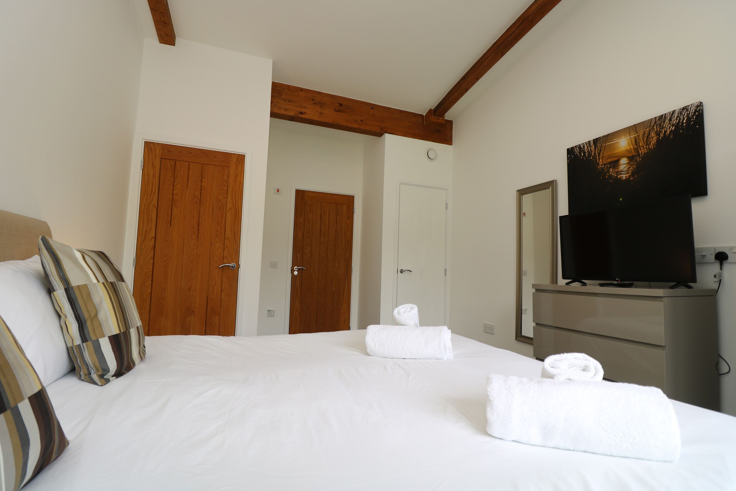 A hotel room with a bed, two wooden doors, a television, and a dresser.