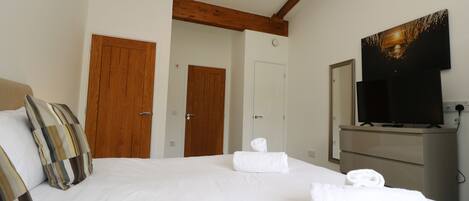 A hotel room with a bed, two wooden doors, a television, and a dresser.
