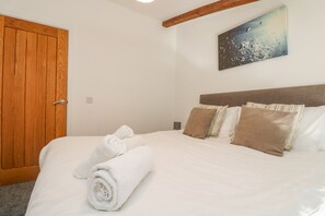 Una cama bien hecha con toallas blancas enrolladas, una puerta de madera y un cuadro del cielo nocturno en la pared.