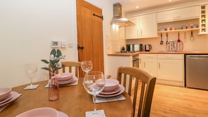Un coin repas avec une table en bois dressée pour quatre personnes, une cuisine avec des placards blancs et une porte en bois.