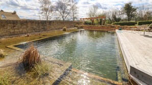 Ein klares Schwimmbecken im Freien mit einer Holzterrasse und Steinmauern.
