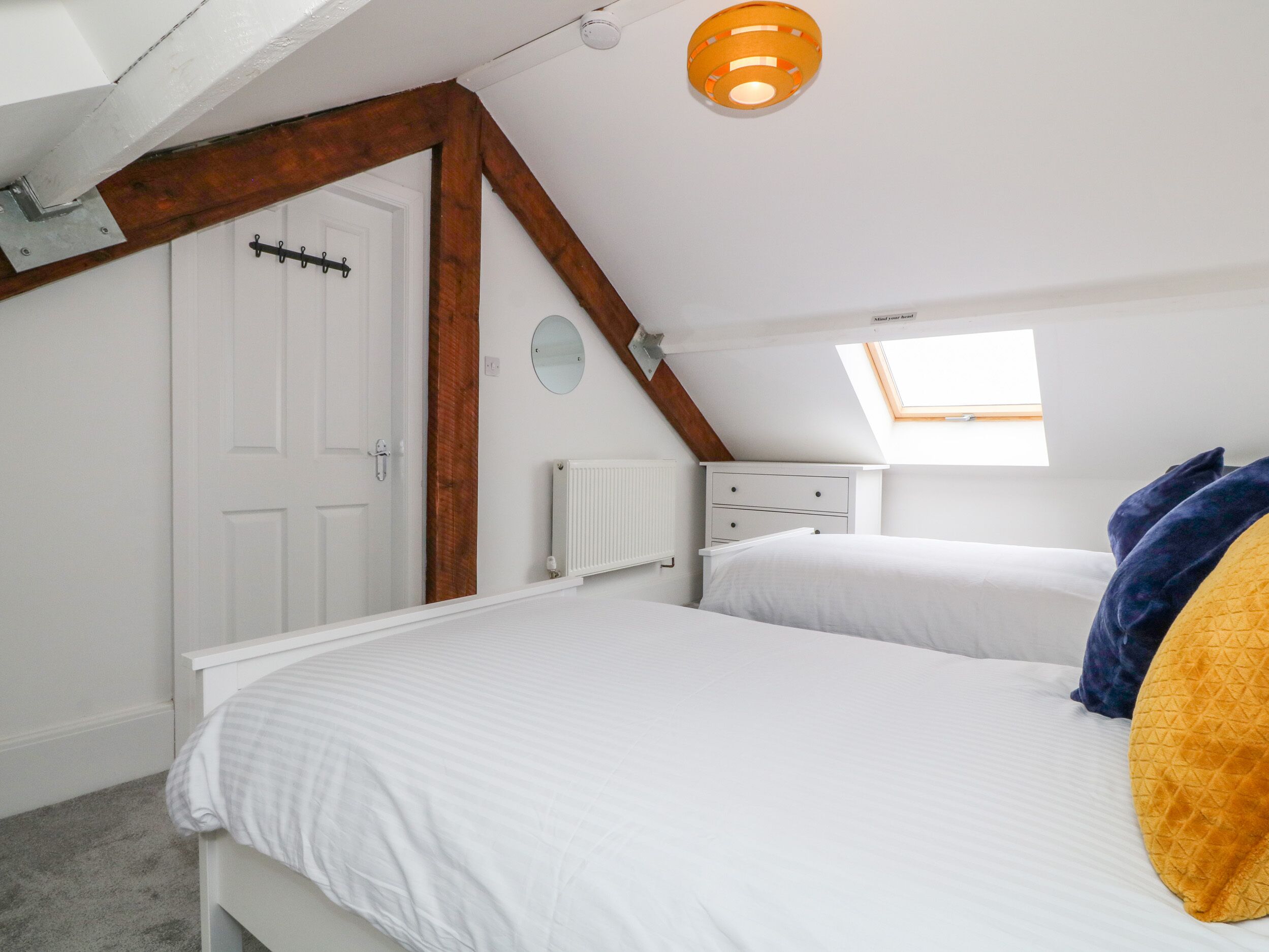 A bedroom with a sloped ceiling, a skylight, a white radiator, and a bed with a white comforter.