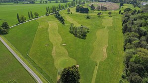 Eine Vogelperspektive auf einen Golfplatz mit gepflegten Fairways, Sandbunkern und einer umliegenden Waldlandschaft.