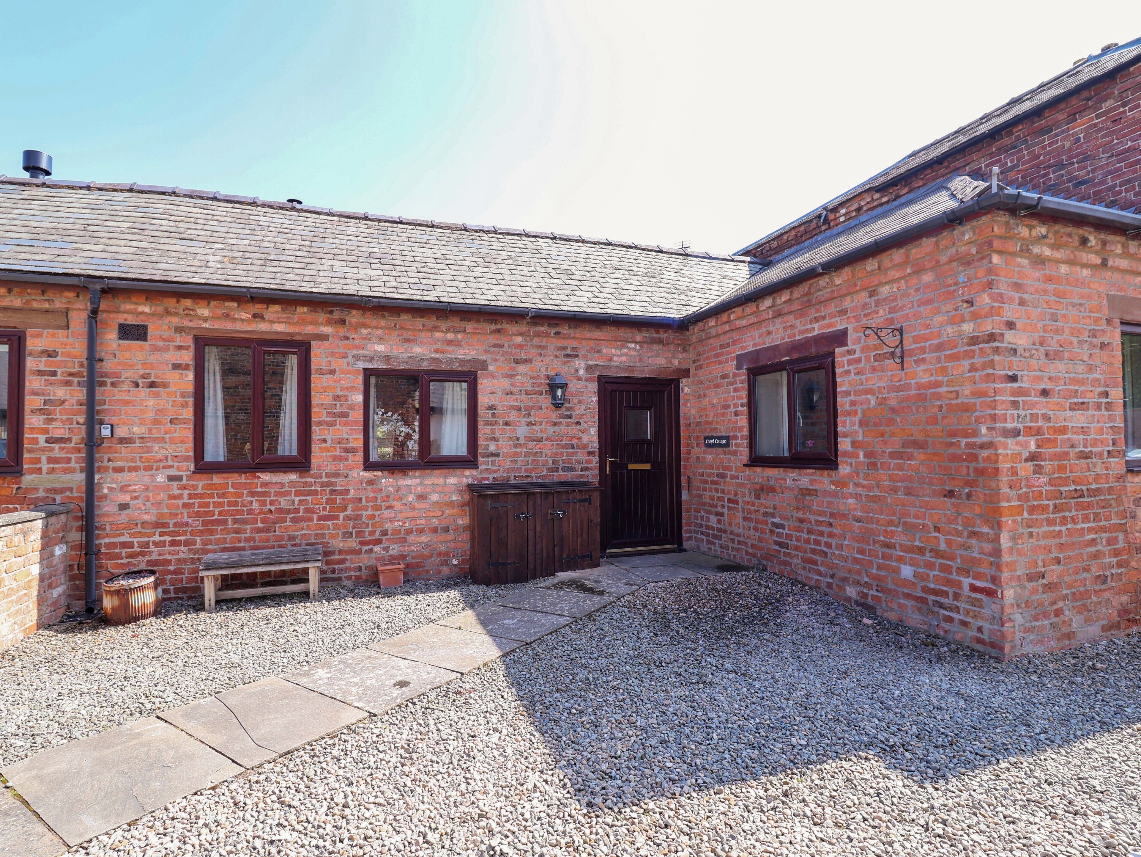 A brick building with a tiled roof, a gravel driveway, and a wooden bench.