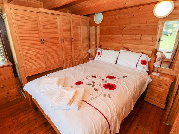 Un dormitorio de madera con una cama grande, un armario, una mesita de noche y un espejo.