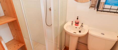 Een badkamer met een douchecabine van glas, een wastafel met zeepdispenser en een toilet.