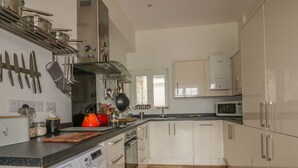 A modern kitchen with white cabinets, a built-in oven, a microwave, and a washing machine. - Cherrywood Manor (Bodmin)
