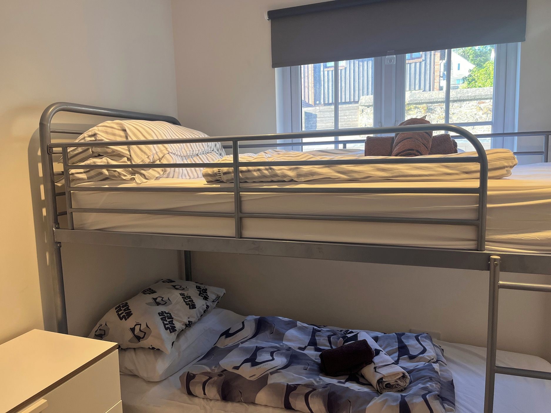 A bunk bed room with a window, a bedside table, and a bed with striped bedding.