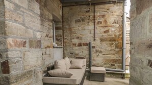A stone-walled room with a wicker sofa and cushions. - Cherrywood Manor (Bodmin)