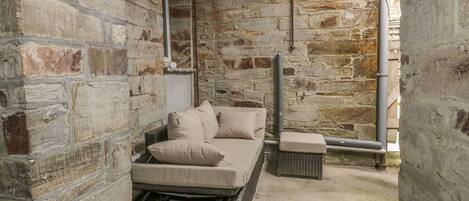 Una habitación con paredes de piedra, un sofá de mimbre y cojines.