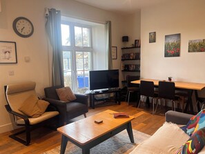 A living room with a sofa, a coffee table, a TV, a bookshelf, and a dining area with chairs. - Cherrywood Manor (Bodmin)
