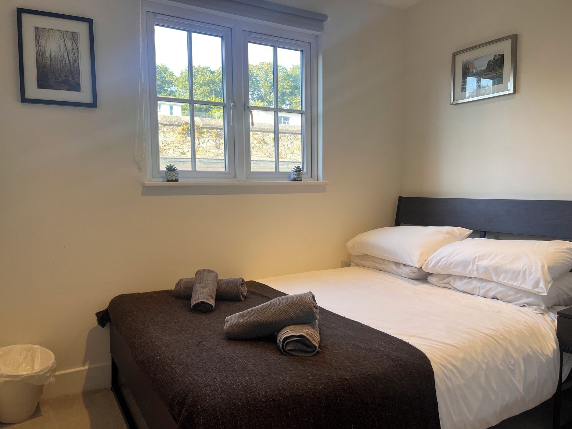 A bedroom with a bed, pillows, a window, and two framed pictures on the wall.