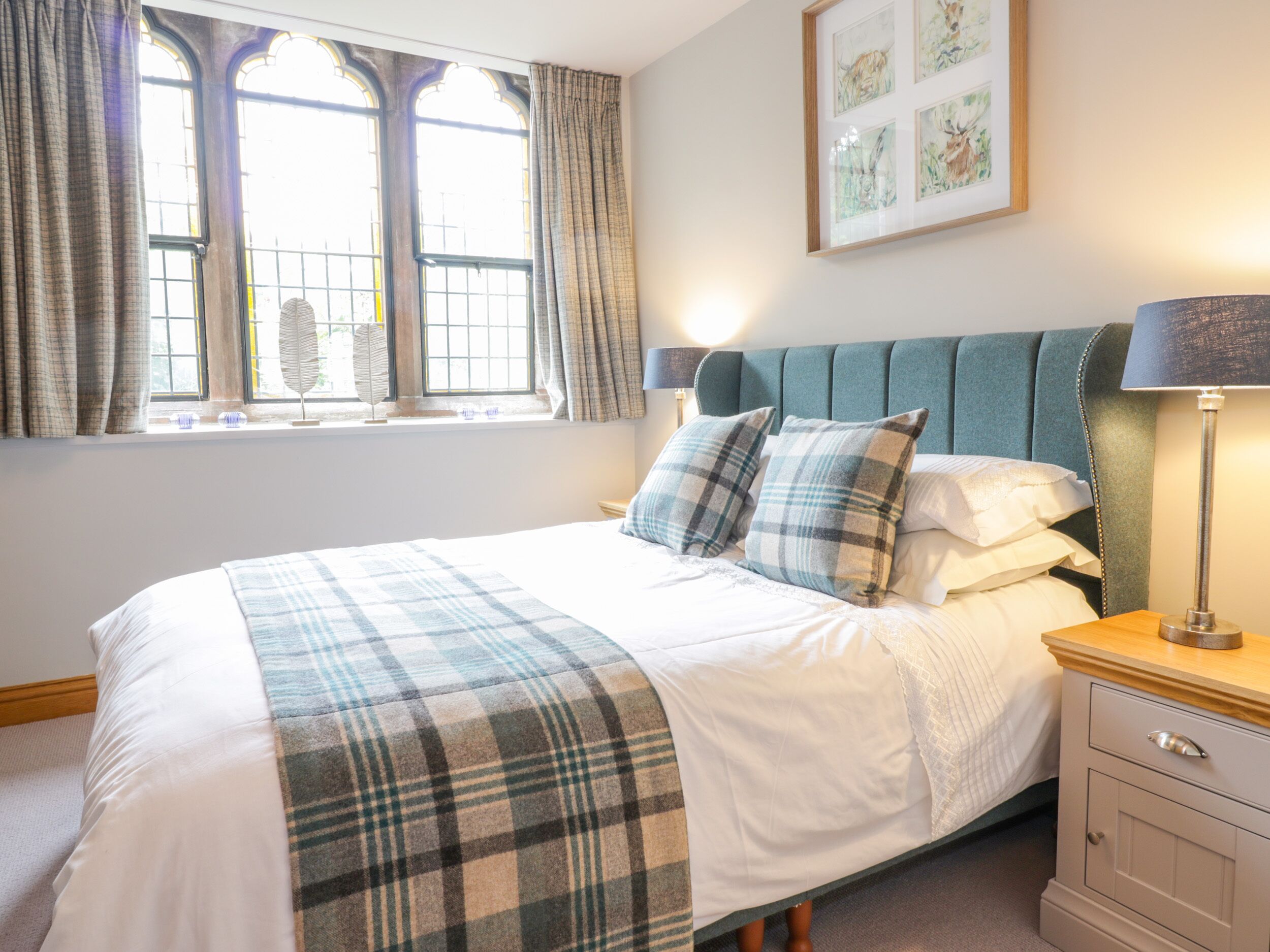 A neatly made bed with a plaid blanket, a headboard, and two bedside lamps.