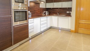 Eine moderne Küche mit Edelstahlgeräten, weißen Schränken und einer Wand in Holzoptik.