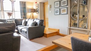 Ein modernes Wohnzimmer mit grauem Sofa, Holztisch und Esstisch. An der Wand hängen gerahmte Bilder und es gibt ein Schrank mit Glastüren.