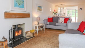Ein gemütliches Wohnzimmer mit Kamin, einer Couch, einem Couchtisch und einer Küche im Hintergrund.