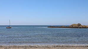 Ein Strand mit ruhigem Wasser, einer Segelyacht und Felsen.